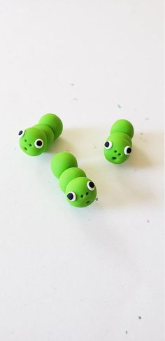 three green toy snakes with googly eyes on a white surface