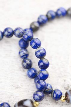 This traditional and bold Dzi bead wrist mala looks amazing on both men and women. Hand strung in Michigan and exclusive to the DharmaShop! Powerful, high-quality, and top grade Lapis beads surround a true agate Dzi bead centerpiece from Taiwan with two gold plated spacers from Thailand. The Dzi bead features a Tiger Tooth design known to energize the wearer as well as attract good luck and health. Tiger Teeth Dzi can assist the owner with concentration, determination, and completion. It is also Lapis Lazuli Gemstone Beaded Bracelets, Lapis Lazuli Beaded Bracelets With Gemstone, Spiritual Lapis Lazuli Round Beads, Hand-strung Lapis Lazuli Beaded Bracelets, Tiger Teeth, Third Eye Chakra Stones, Tiger Tooth, Tooth Design, Wrist Mala