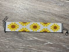 a yellow and white beaded key chain with sunflowers on it, sitting on a wooden surface