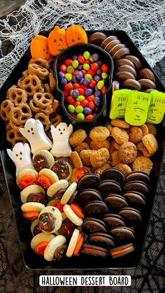 a black tray filled with halloween treats and candies on top of a lace table cloth