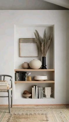 a shelf with books, vases and other items on it in front of a white wall