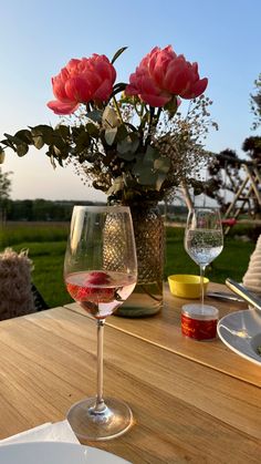 two wine glasses sitting on top of a wooden table next to a vase filled with flowers