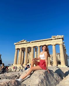 a woman sitting on top of a rock in front of the parthenion temple