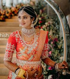 a woman in an orange and red bridal outfit standing next to some stairs with flowers