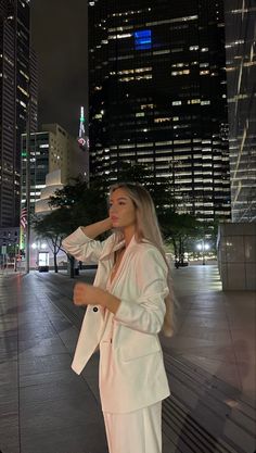 a woman standing in the middle of a city at night wearing a white suit and heels