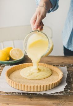 someone pouring batter on top of a tart shell with lemons in the background