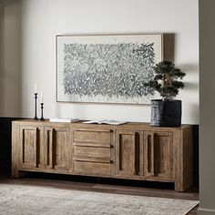 a living room with a large painting on the wall next to a wooden sideboard