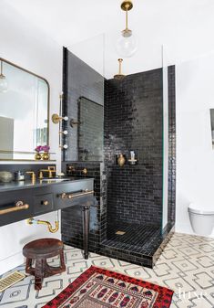 a black tiled bathroom with gold fixtures and mirrors on the wall, along with an antique stool