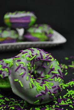 green and purple sprinkled doughnuts sitting on top of each other next to plates