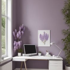 a desk with a computer and potted plants in front of a purple painted wall