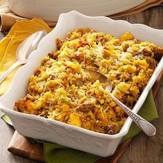 a casserole dish with meat and cheese in it on a wooden board next to a serving spoon