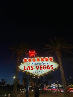 the famous las vegas sign is lit up at night with palm trees and buildings in the background