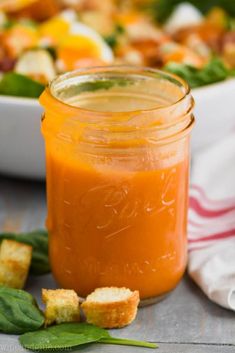 an orange sauce in a glass jar next to bread croutons and spinach leaves