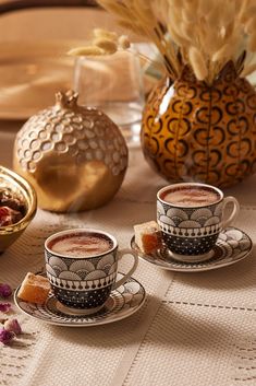 two cups and saucers sitting on top of a table next to some dried flowers