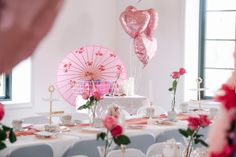 the table is set with pink and white decorations, including two heart - shaped balloons