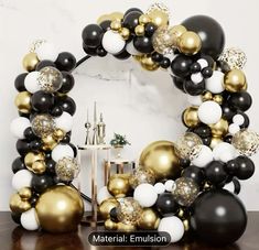 black, white and gold balloons are arranged in the shape of a wreath on a table