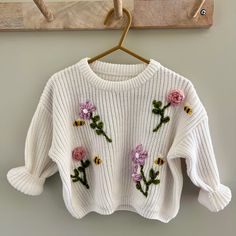 a white sweater with flowers on it hanging from a hook