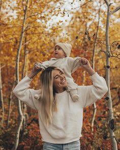 a woman holding her child up in the air while standing next to trees with leaves on them