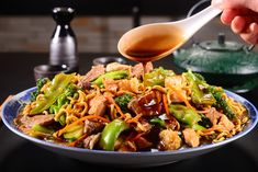 someone pouring sauce over a plate of noodles and vegetables