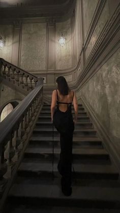 a woman is walking up the stairs in a dark room with chandeliers on either side