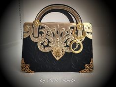 a black and gold handbag with ornate designs on the front, sitting on a white surface