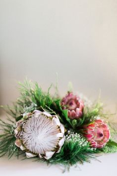 a bouquet of flowers sitting on top of a white table next to a vase filled with green and pink flowers