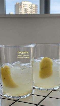 two glasses filled with liquid sitting on top of a tiled counter next to a window