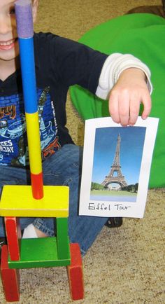 a young boy sitting on the floor playing with wooden blocks and a picture of the eiffel tower