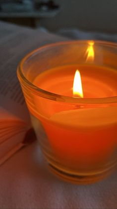 a lit candle sitting on top of a table next to an open book in front of it