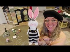 a woman wearing glasses and a hat is holding a stuffed rabbit in front of her