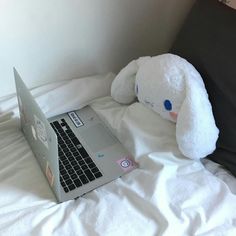 an open laptop computer sitting on top of a bed with a stuffed animal next to it