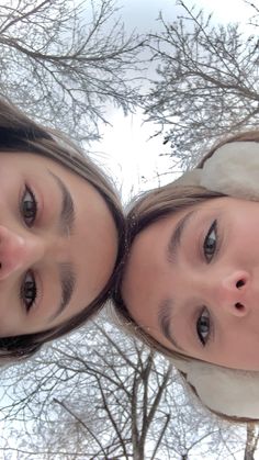 two young women standing next to each other in front of some trees and snow covered branches