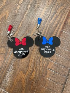 two mickey mouse keychains with red, white and blue bows are on a wooden surface