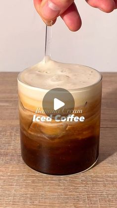 someone is dipping something into a cup with ice coffee in it on a wooden table