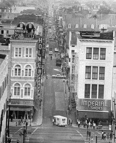 black and white photograph of an old city street with cars, pedestrians, and buildings