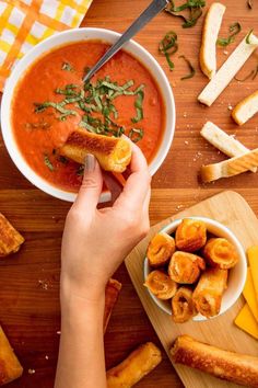 a person holding a piece of bread over a bowl of soup on a cutting board