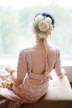 a woman sitting on top of a bed wearing a flower in her hair and looking out the window