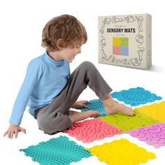 a young boy sitting on the floor playing with an assortment of colorful mats in front of him