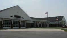 an empty parking lot in front of a large white building with flags flying from it's sides