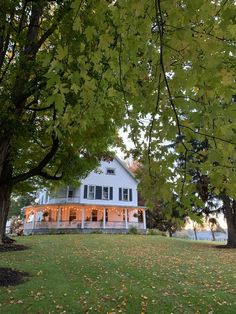 a large white house sitting on top of a lush green field next to trees and leaves