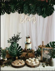 a table topped with cakes and cupcakes next to greenery