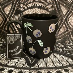 a black coffee mug with skulls and leaves on it, next to a card that says halloween