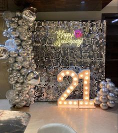 a table topped with balloons and lights next to a number 21 sign in front of a mosaic wall