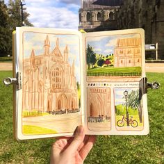 someone is holding an open book with drawings on it in front of a large building