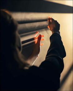 a woman is looking through blinds at the light coming in from behind her and reaching for something