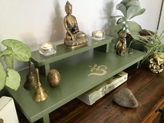 a green table with candles and statues on it next to a potted houseplant