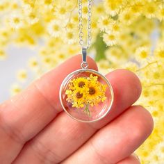 A beautiful sunflower themed pendant encased in a sterling silver round frame. The pendant is the perfect way to send someone special a bunch of bright, beautiful sunflowers. The sunflower pendant features a tiny, bunch of sunflowers, design surrounded by real pressed Queen Anne's Lace flowers preserved in resin.  Please note that the sunflowers themselves are not real pressed flowers. The pendant measures approximately 20mm in width and height excluding the bail.  The pendant is further decorat Sunflower Design Jewelry For Mother's Day, Elegant Round Sunflower Jewelry, Elegant Round Sunflower Design Jewelry, Elegant Round Jewelry With Sunflower Design, Sunflower Design Flower Jewelry For Anniversary, Silver Sunflower Pendant Jewelry, Sunflower Design Jewelry For Anniversary, Silver Jewelry With Sunflower Design Flower Pendant, Mother's Day Sunflower Design Jewelry