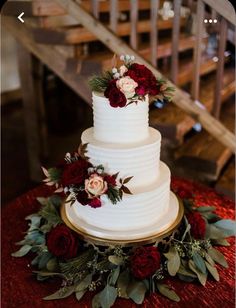 a three tiered white wedding cake with red flowers and greenery on the side