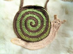 a crocheted bag with a snail on the front and side, sitting on a white furnishing