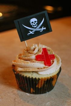 a cupcake with a red cross on top and a pirate flag sticking out of it